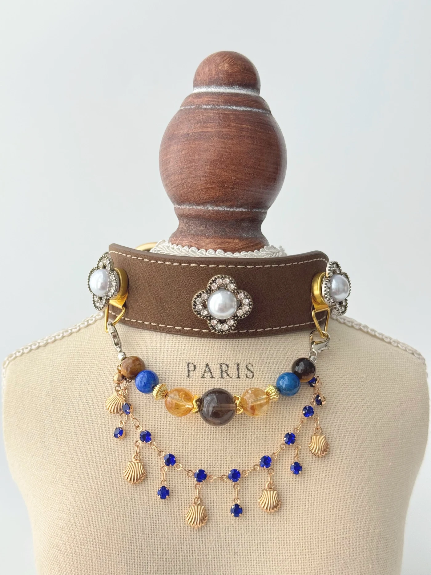 Braunes Golden Quartz Double Strand Halsband auf einem Ständer mit perlenartigen Blüten sowie blauen und goldfarbenen Schmuckketten