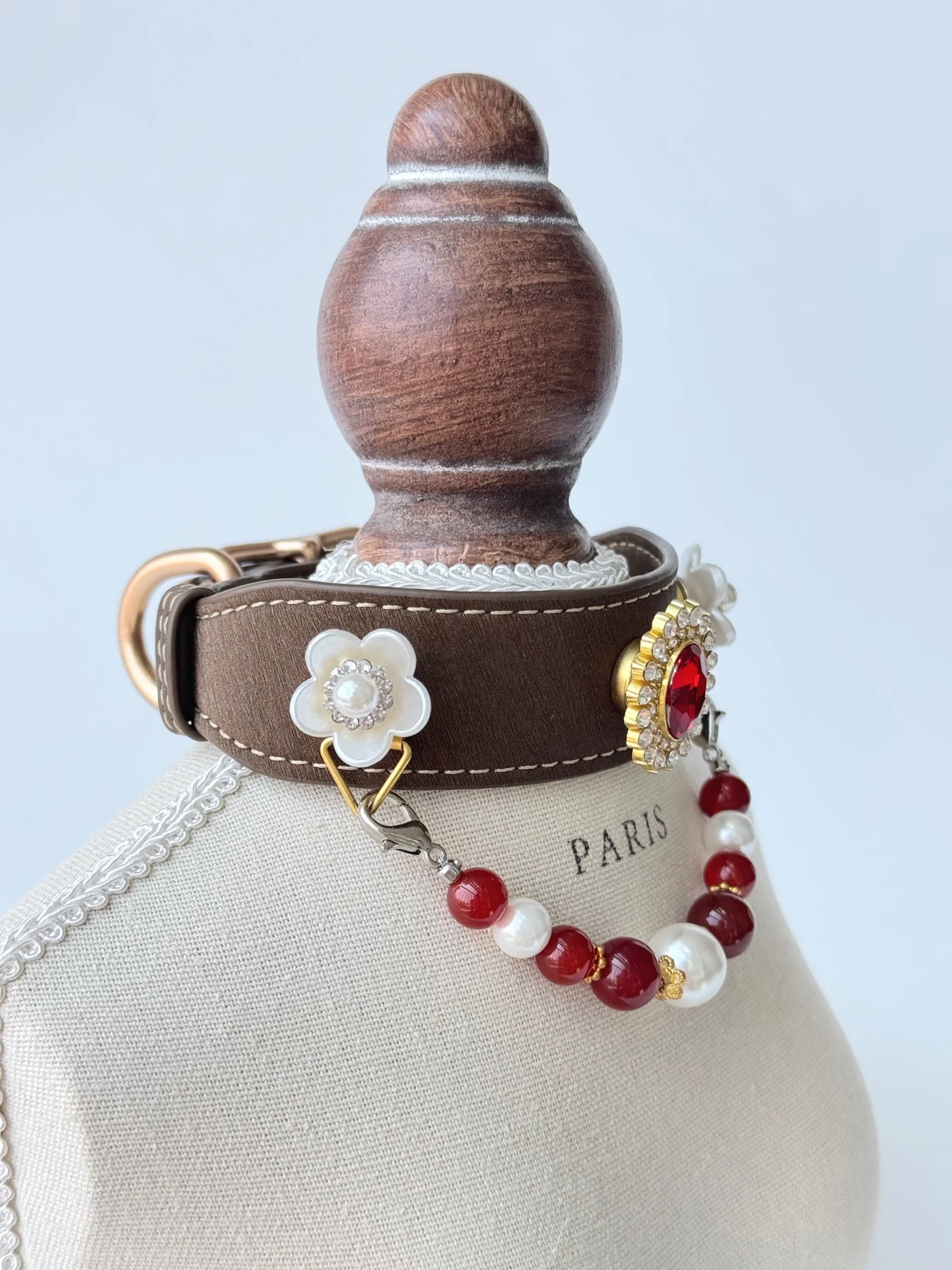 Braunes Scarlet Pearl Halsband auf einem Ständer mit weißen Blüten und rot-weißen Perlen